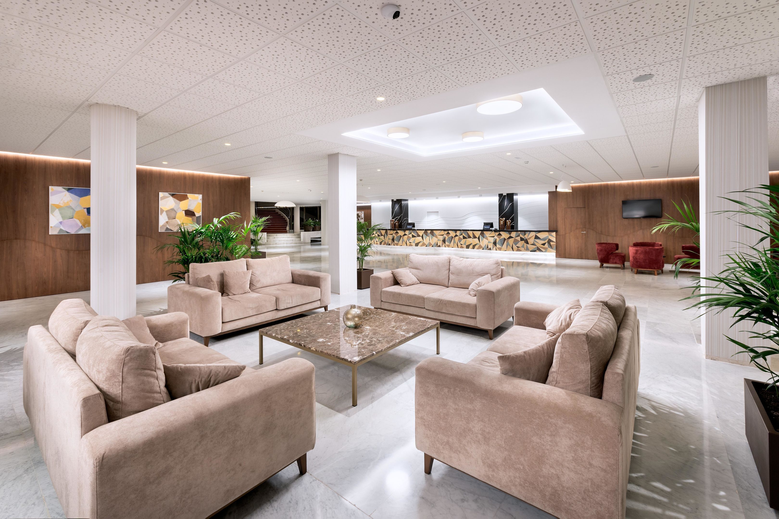 Un vestíbulo amplio con sofás color beige, una mesa de centro y una zona de recepción al fondo.