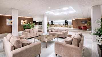 Un vestíbulo amplio con sofás color beige, una mesa de centro y una zona de recepción al fondo.