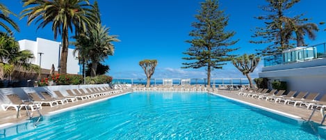 A clear blue pool with lounge chairs and palm trees.