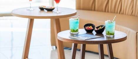 A modern room with a round wooden table and a sofa, both with a light wood finish. There are two glass tables with drinks and bowls on them.