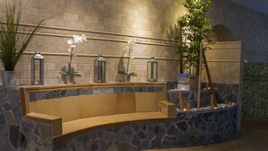 Un banc en pierre agrémenté d’un jardinier, de plantes en pot et de lanternes, le tout adossé à un mur carrelé.