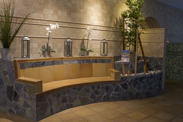 Een stenen bank met een plantenbak, potplanten en lantaarns tegen een betegelde muur.