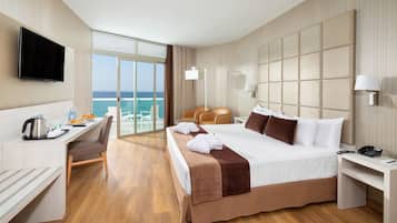 Een hotelkamer met een bed, een bureau, een stoel, een televisie en uitzicht op de oceaan.