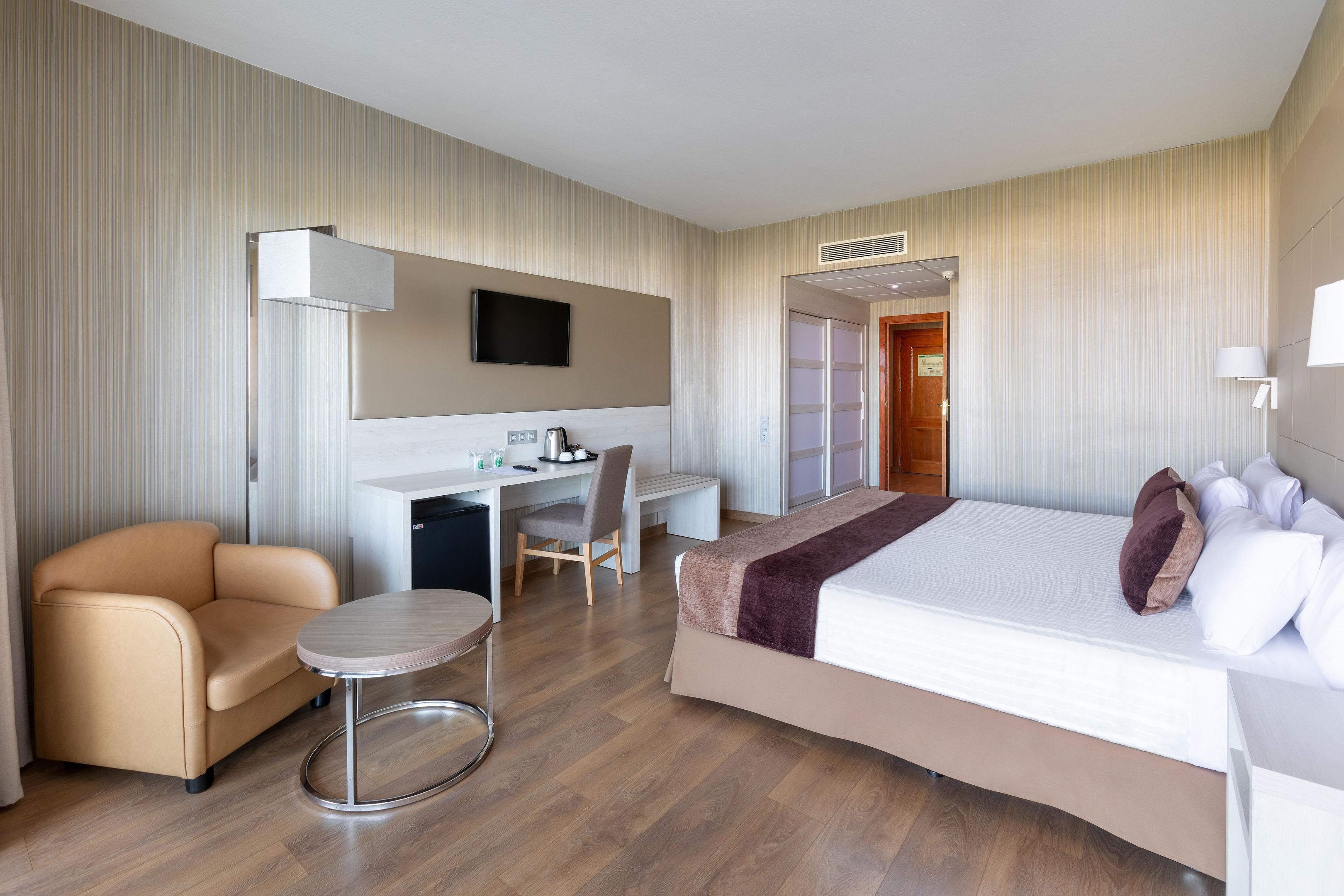 A hotel room with a bed, a desk, a chair, and a small round table.