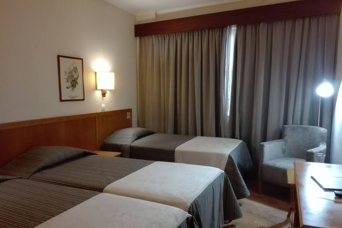 A hotel room with two beds, a desk, a chair, and a lamp.