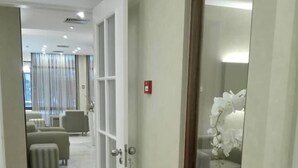 A hotel corridor with a wooden floor, a white door, and a view into a living area with a sofa and a coffee table. - Hotel Do Centro (Funchal)