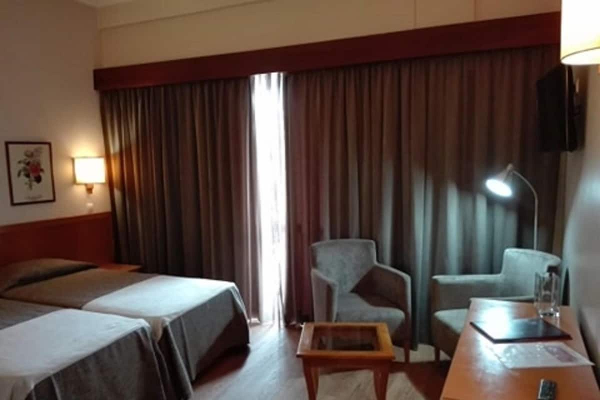 A hotel room with two beds, a desk, a chair, a lamp, and a picture on the wall.
