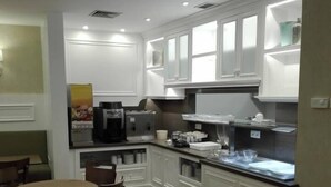 A modern kitchen with white cabinetry, a dining area with wooden chairs, and a coffee machine. - Hotel Do Centro (Funchal)