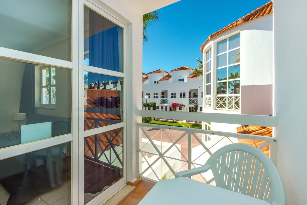 A balcony with a white chair, a table, and a view of a white building with red-tiled roofs.