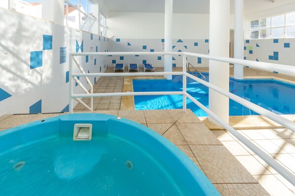 An indoor swimming pool with a hot tub, tiled walls, and sunlit areas with lounge chairs. - Apartamentos Turísticos Club Ouratlântico (Albufeira)