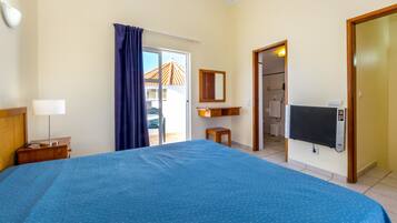 A hotel room with a large bed, a desk with a lamp, a TV, and a bathroom visible through an open door.