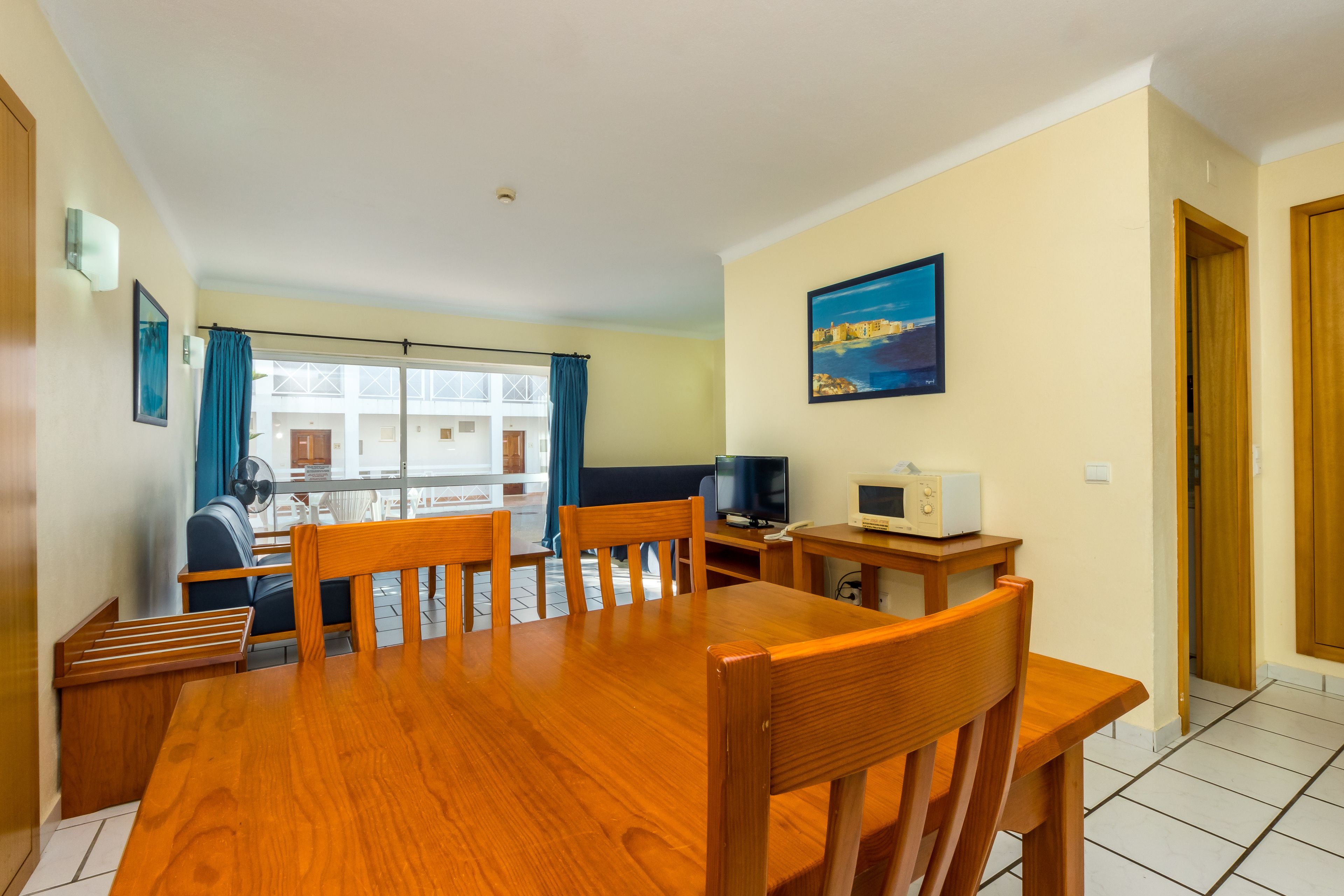 Un comedor con mesa y sillas de madera, televisor, microondas y ventana con cortinas.