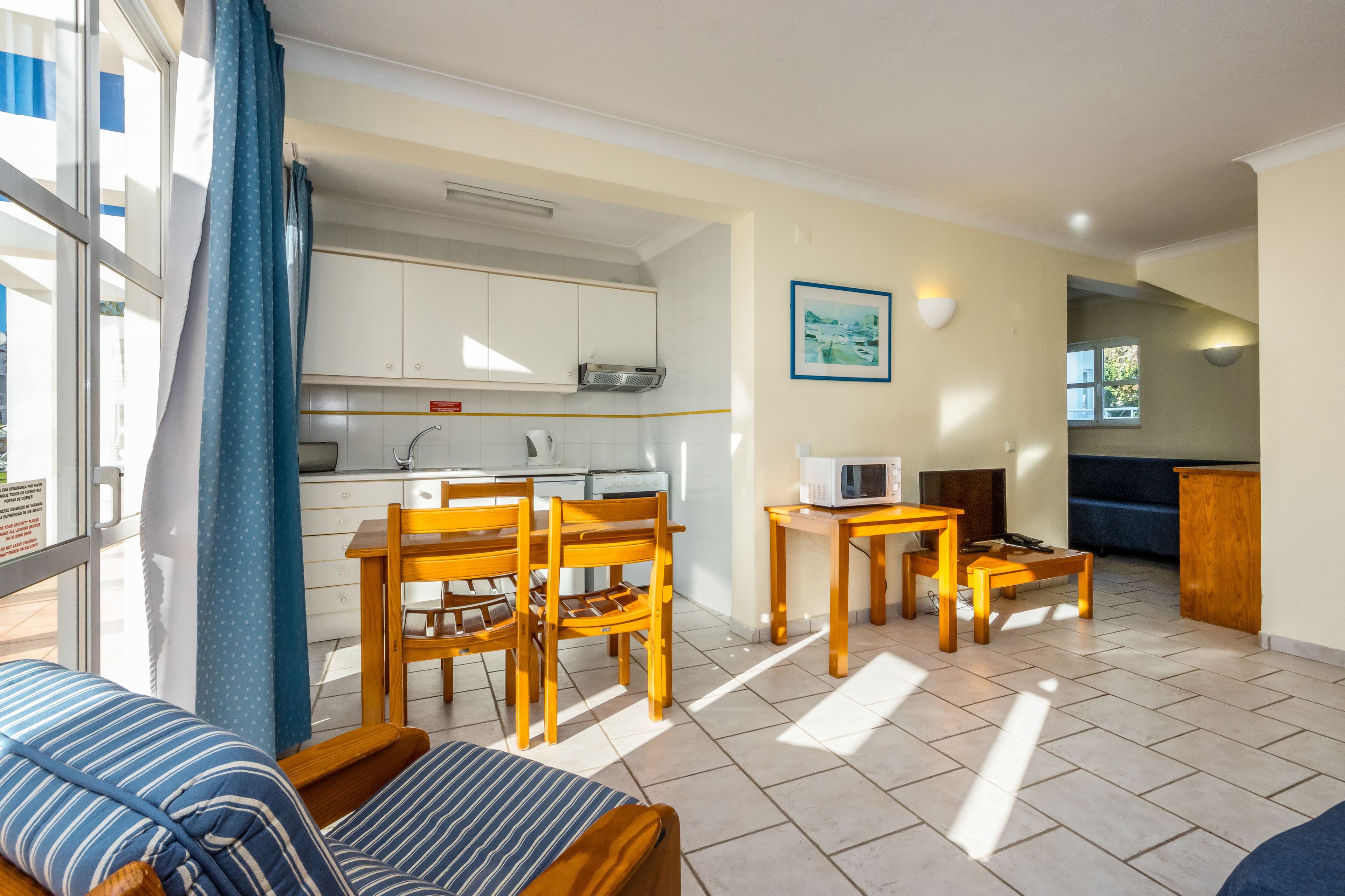 A compact living space with a kitchenette, a dining area with wooden furniture, and a view through a window.