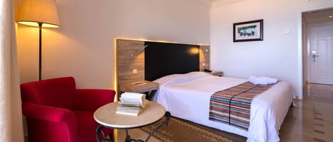 Une chambre d’hôtel avec un lit, un fauteuil rouge, une petite table avec une lampe et un tableau au mur.