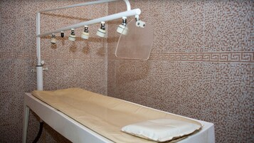 Una cama de hospital con colchón y almohada blancos, un riel superior blanco con panel transparente, y una pared con azulejos estampados.