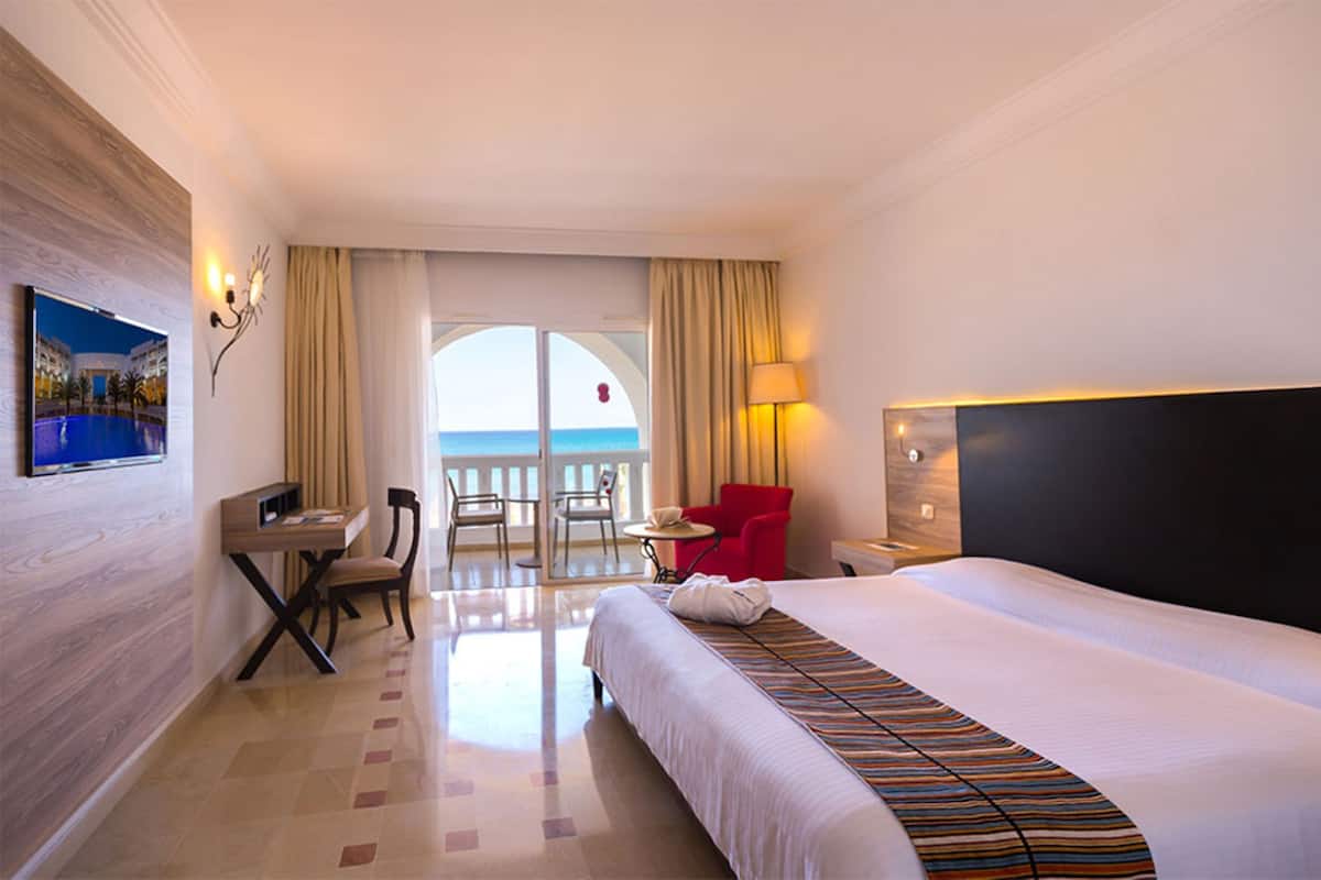 Una habitació d'hotel amb llit, escriptori, cadira, televisió i vista al mar.