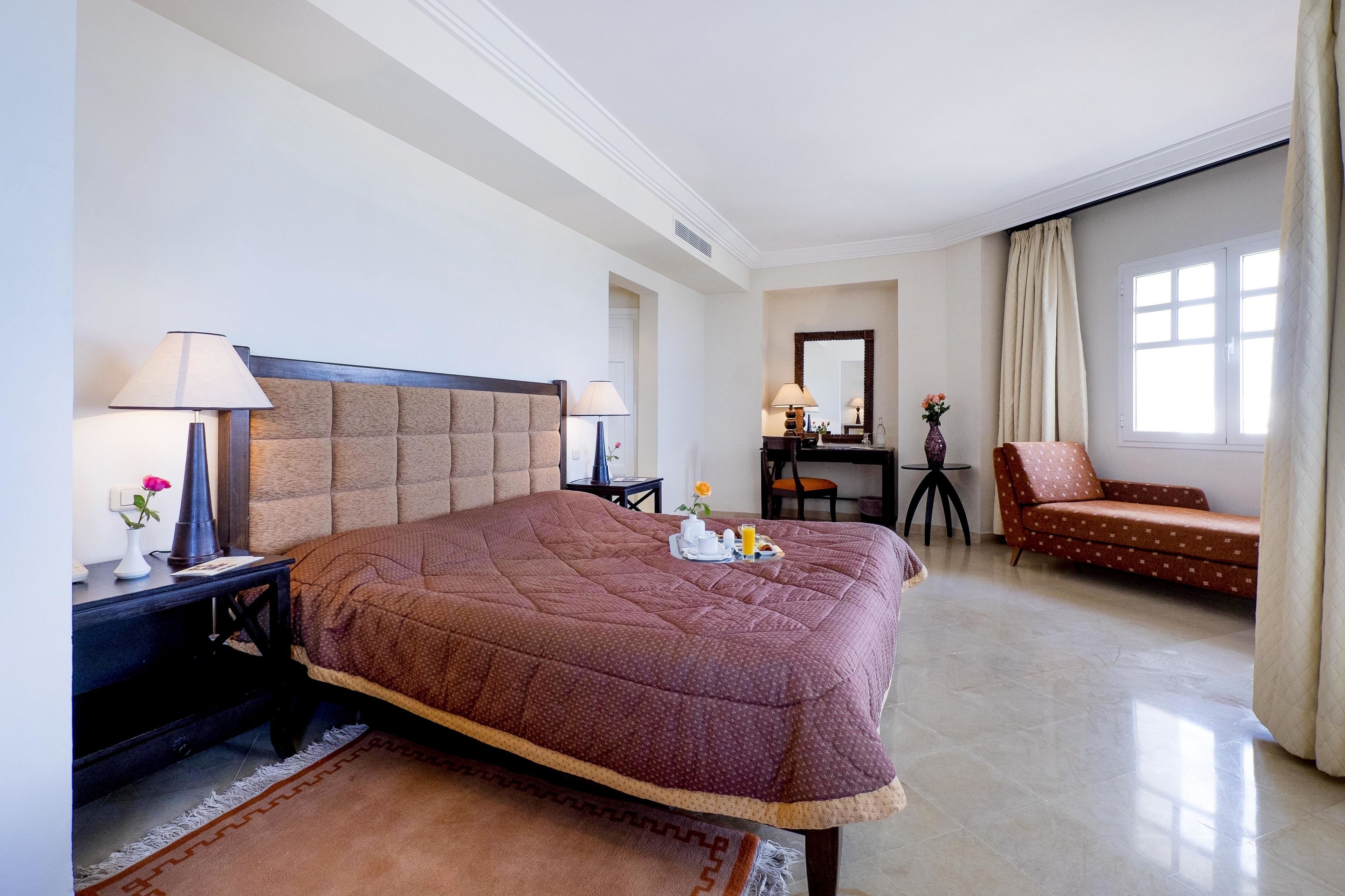 A hotel room with a large bed, a desk with a chair, a sofa, and a window with curtains.