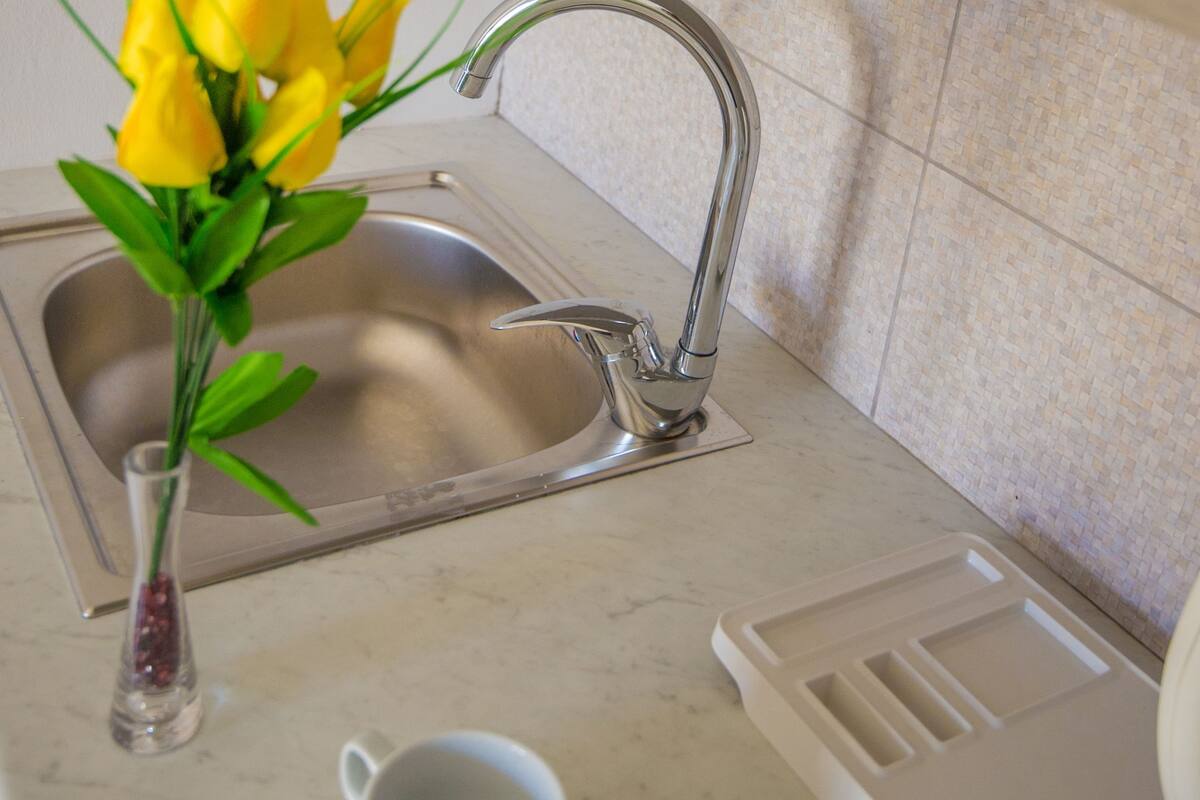 Una cocina con un lavabo, una taza en la encimera y un florero con flores amarillas.