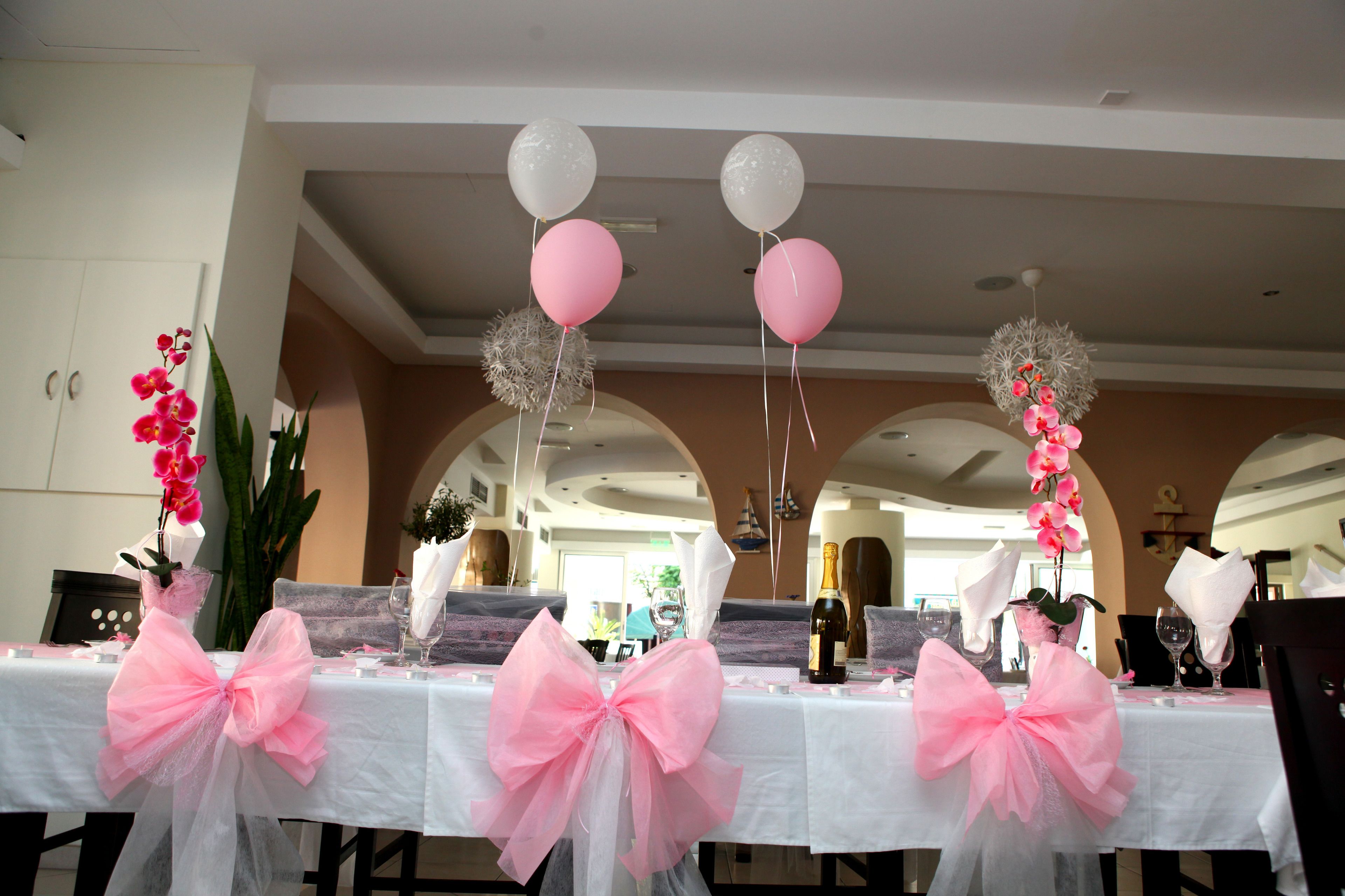 A dining table with pink bows, white tablecloth, and balloons.