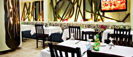 A restaurant with tables set for dining, chairs, and a television on the wall.