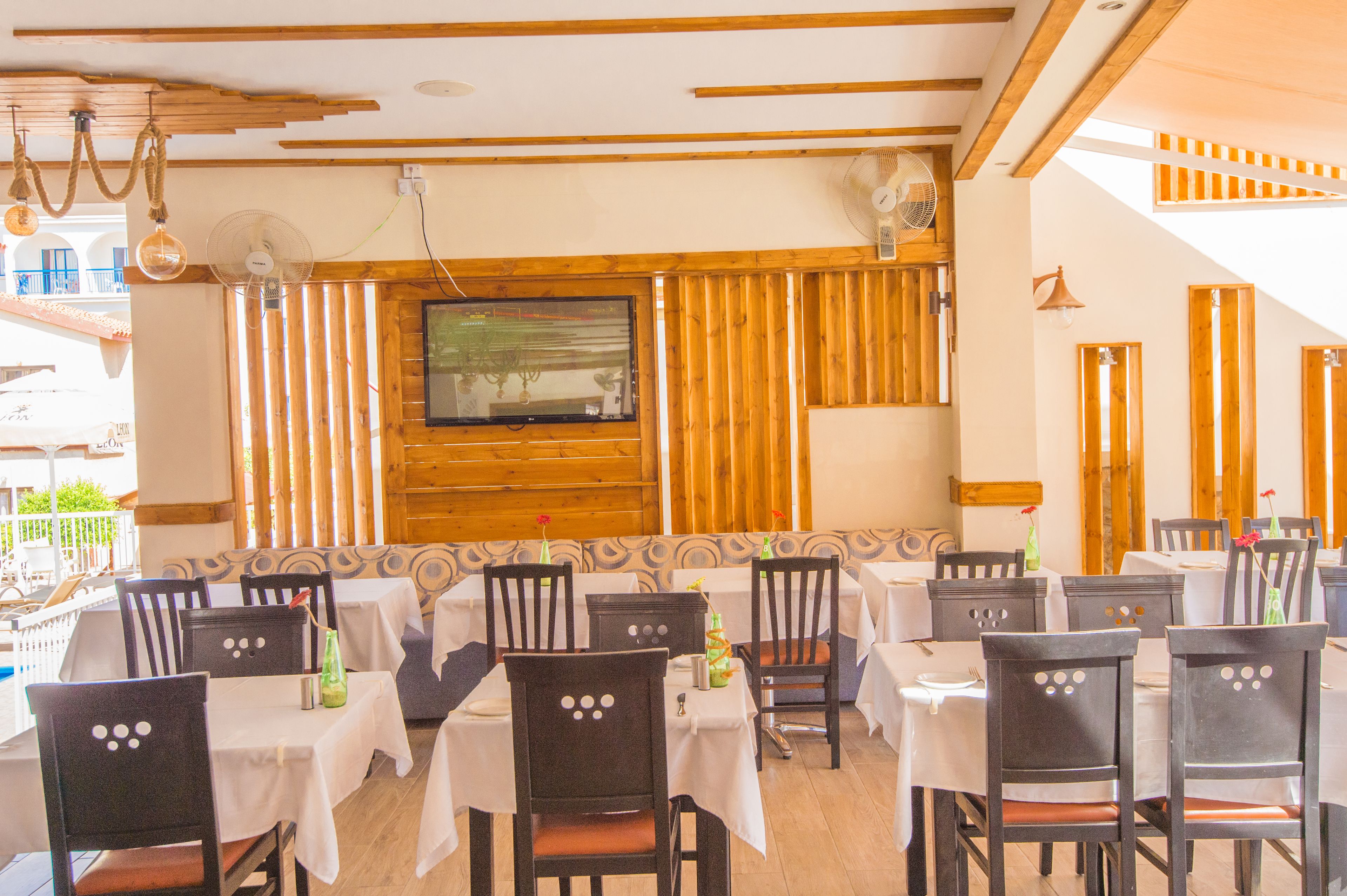 Un restaurante con varias mesas y sillas, paneles de madera y un televisor en la pared.