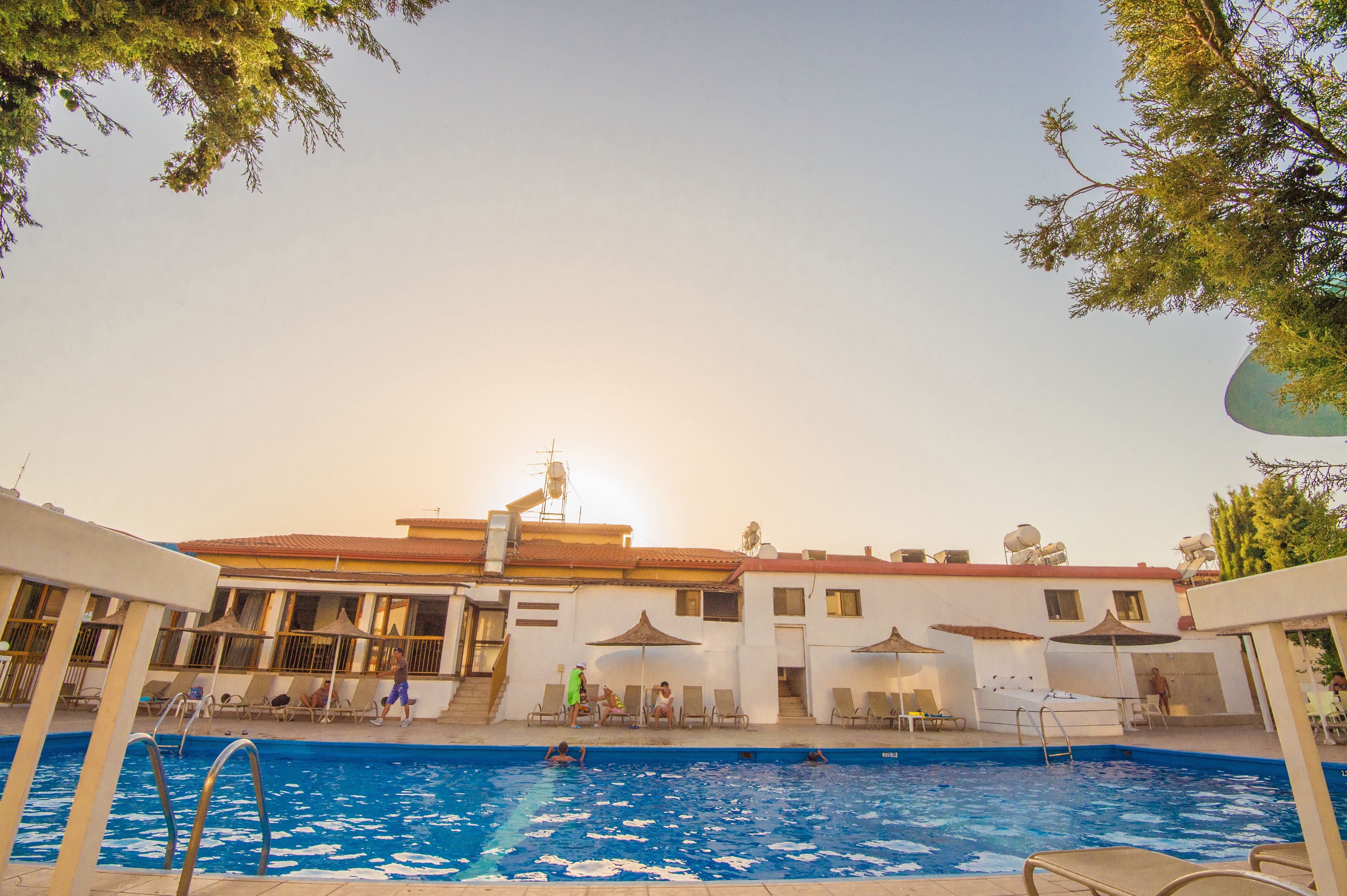 A swimming pool area with lounge chairs and umbrellas, a building with a red roof, and a clear sky.
