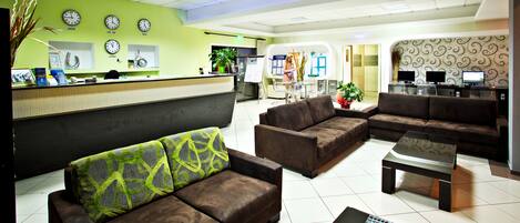 En hotellobby med en receptionsdisk, en sittgrupp och en datorarbetsplats.