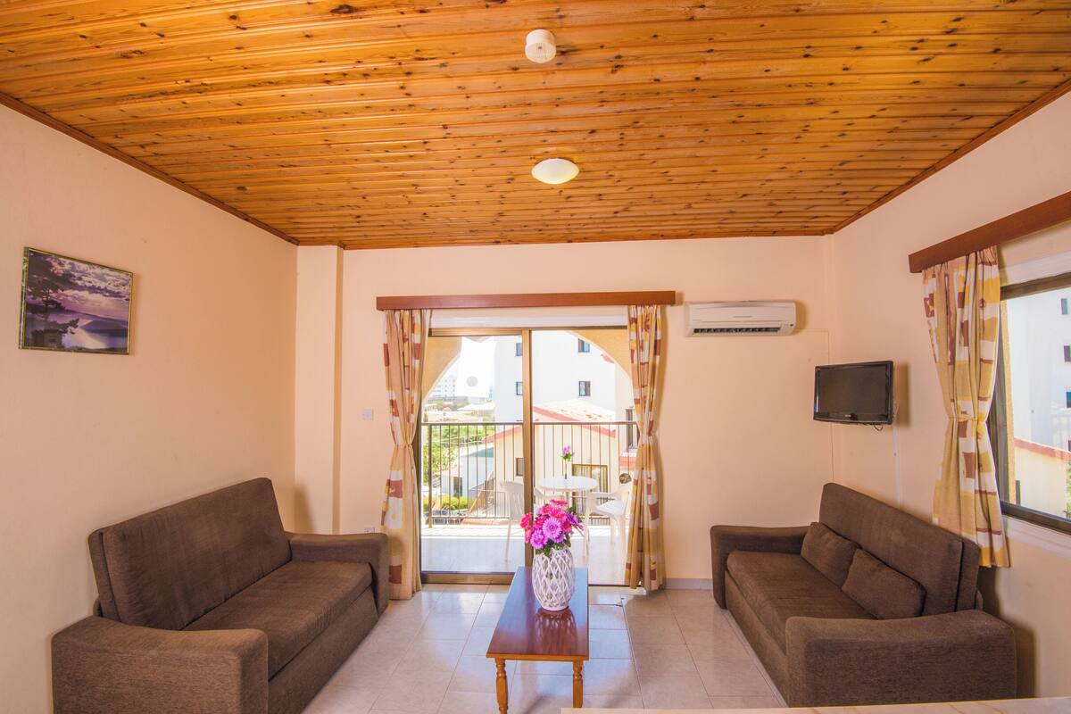 Un salón con dos sofás, techo de madera, una mesa con un jarrón y vistas a través de un ventanal.
