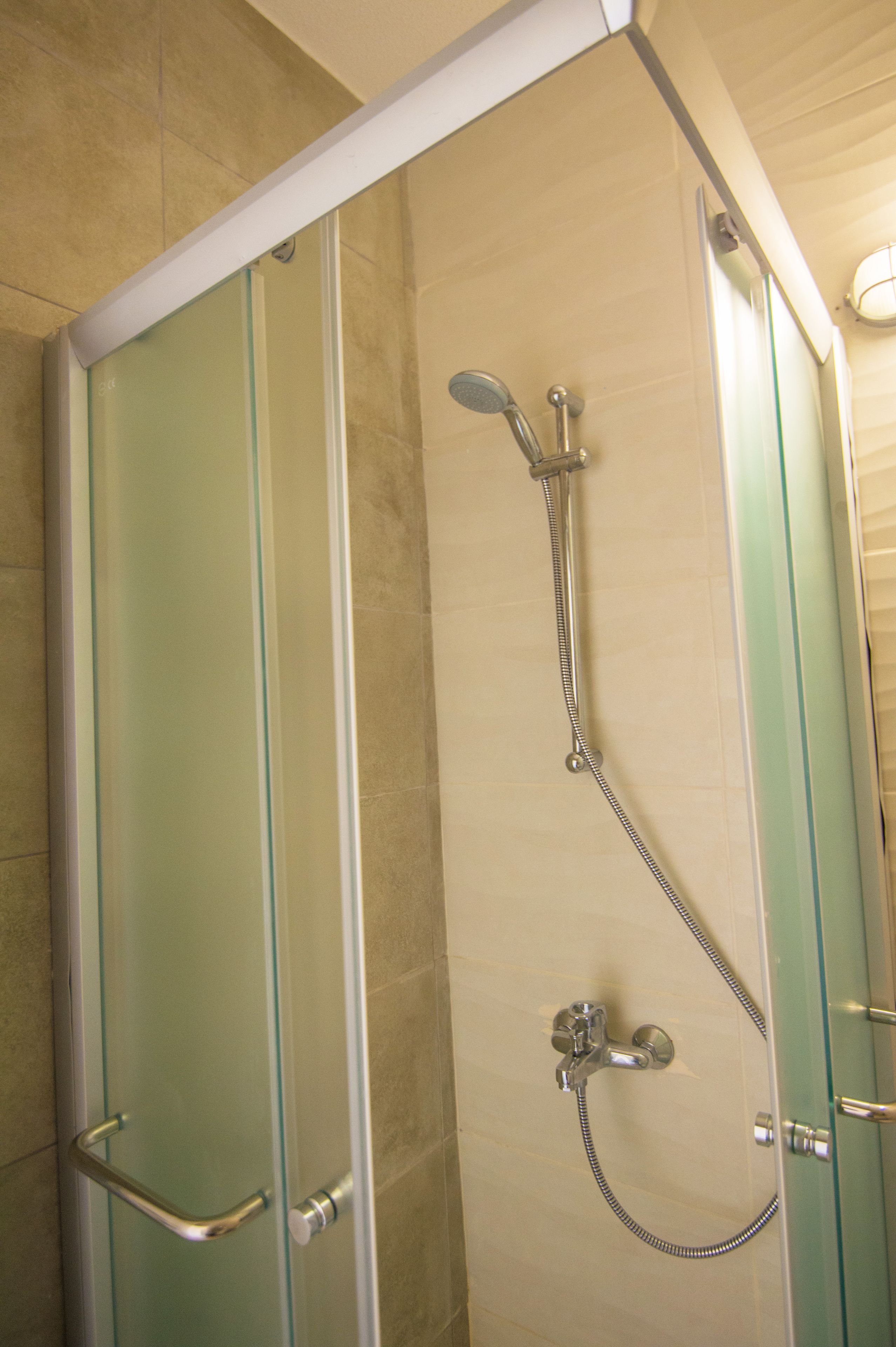 Une douche fermée par des parois en verre, dotée d’un pommeau de douche à main et d’un flexible à main.