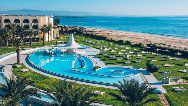 Un complexe hôtelier doté d’une grande piscine, d’une plage et de palmiers.