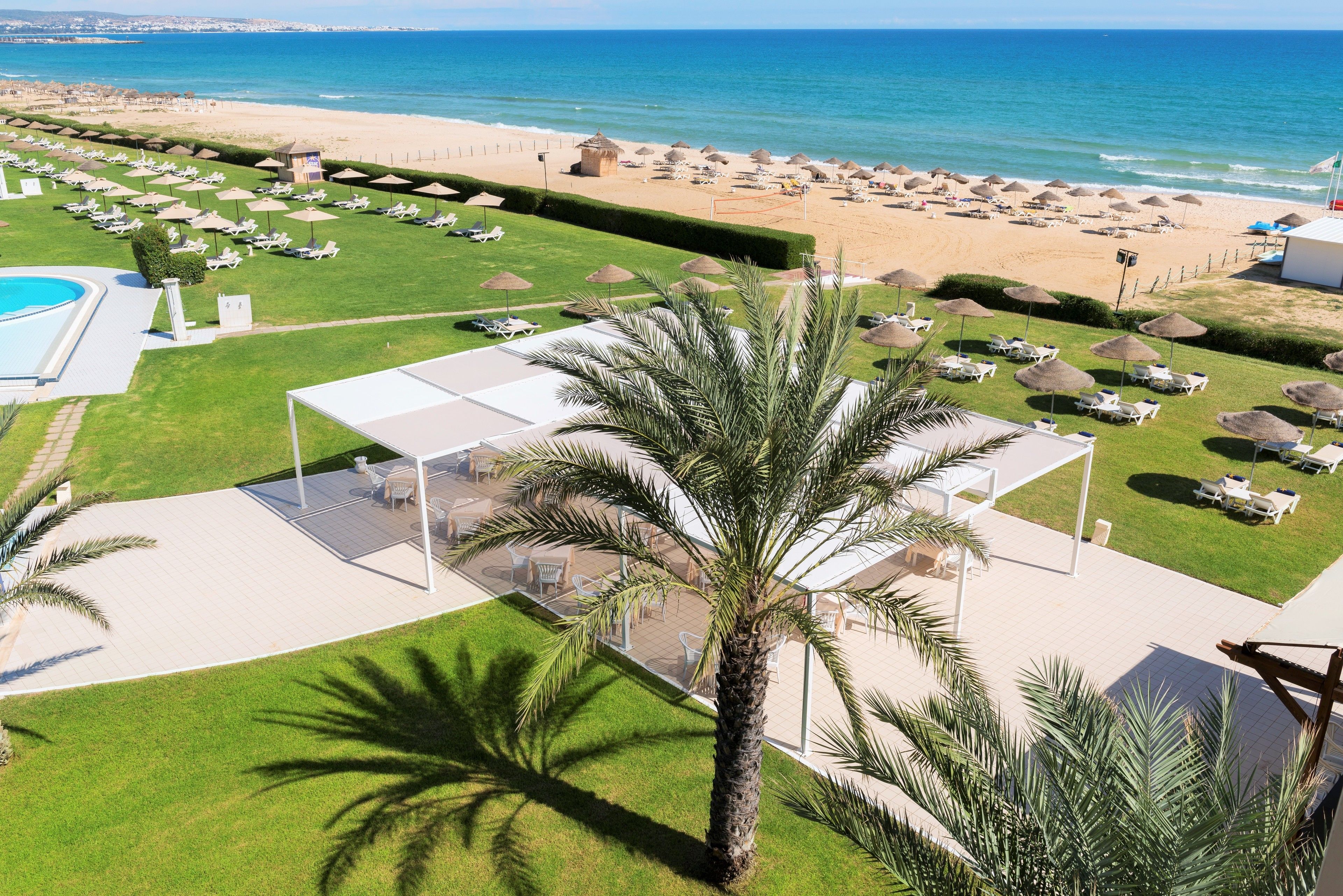 A resort with a pool, sun loungers, umbrellas, and a beach view.