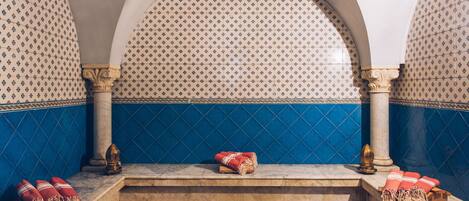 A traditional Moroccan riad with a tiled wall, a marble bench, and a small wooden table with cushions.