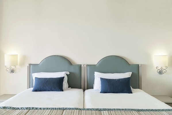 A double bed with two pillows, a headboard, and two wall-mounted lamps.