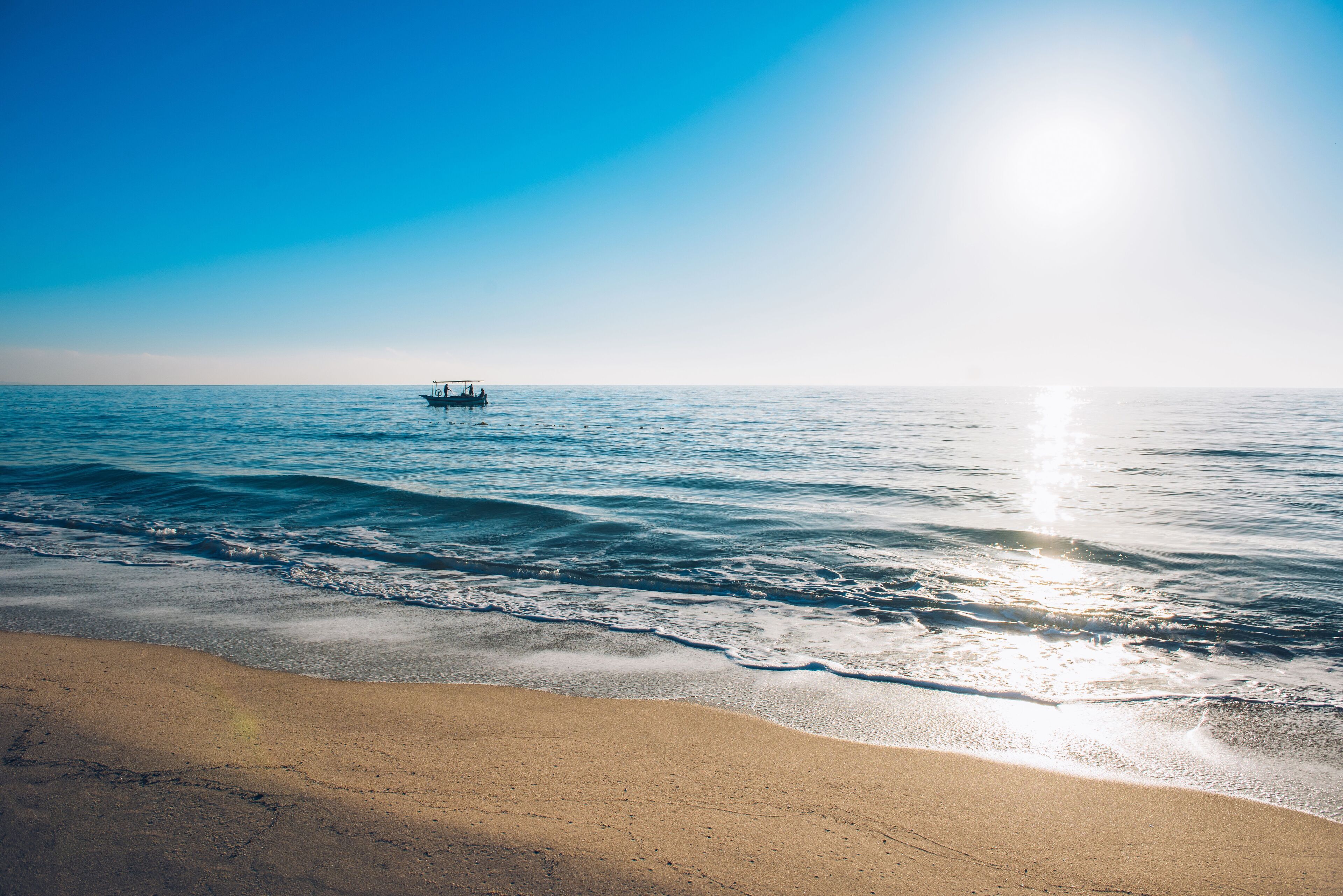 A beach with a boat in the distance and a clear sky.