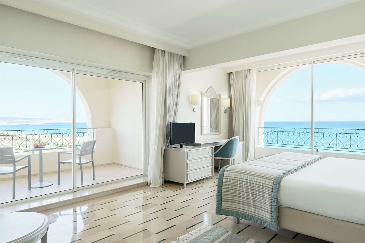 Een hotelkamer met balkon, een bed, bureau, televisie en stoel.