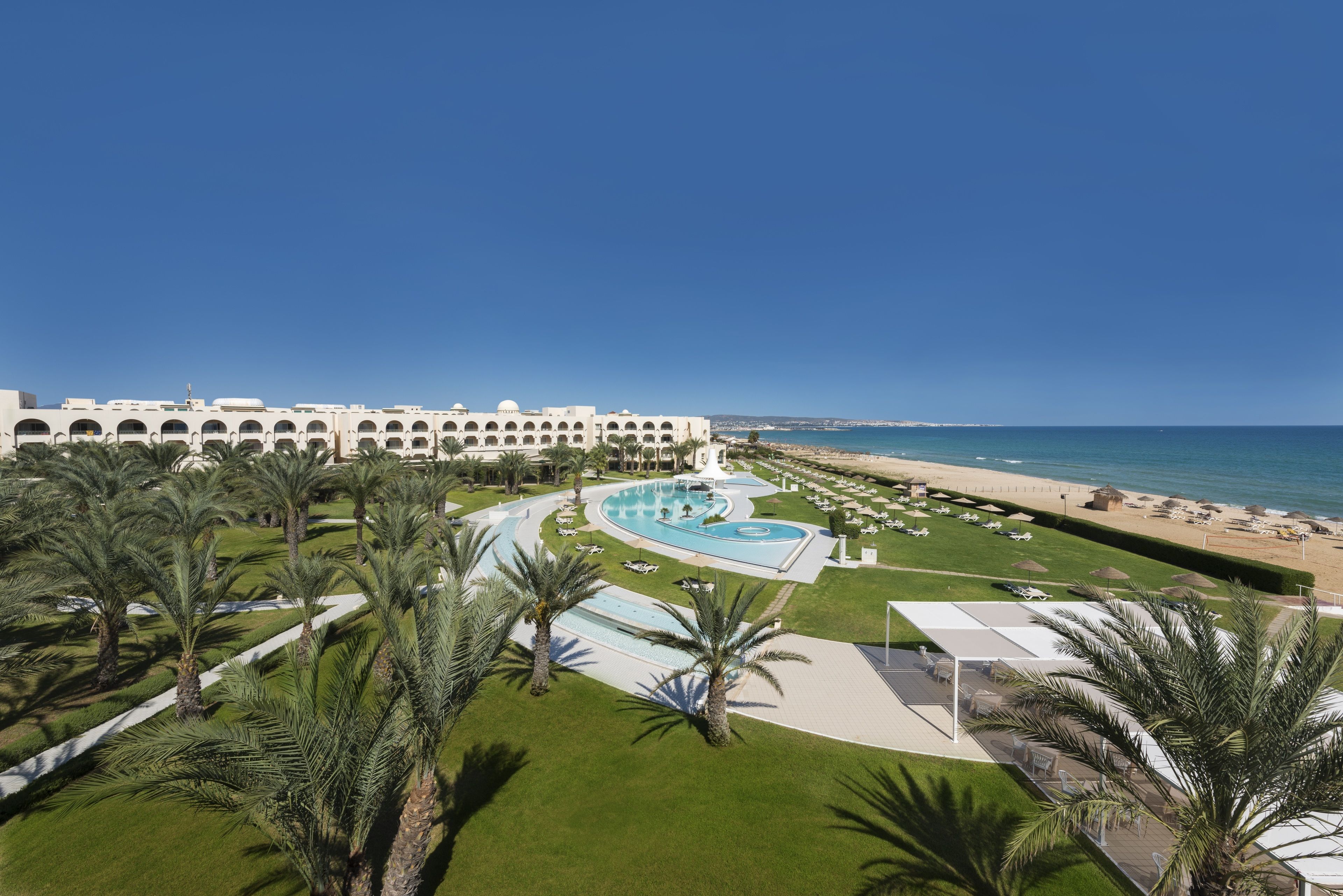 Un resort con piscina, palmeras y vista al mar.