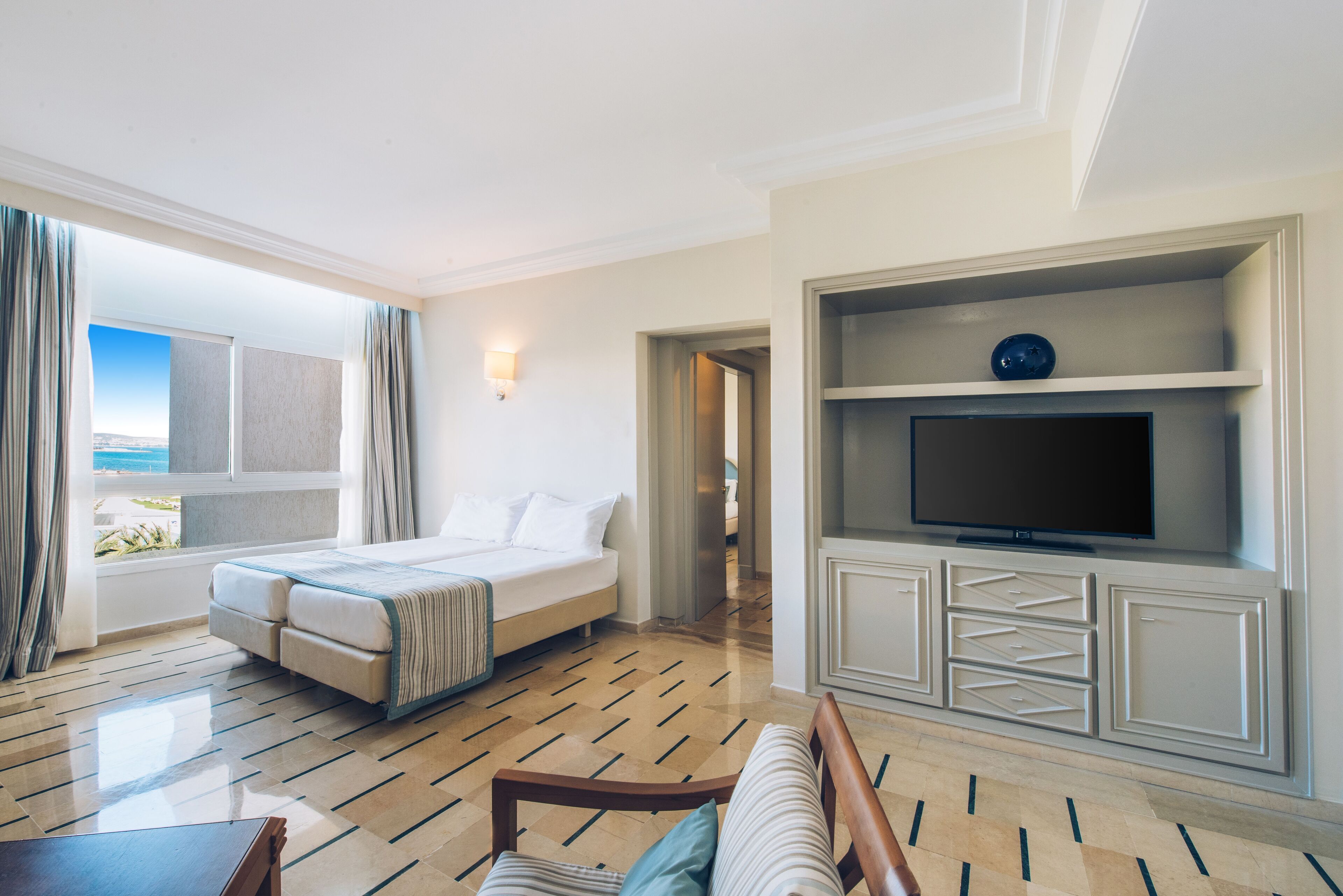 A hotel room with a bed, a TV, a sofa, and a view of the outdoors.