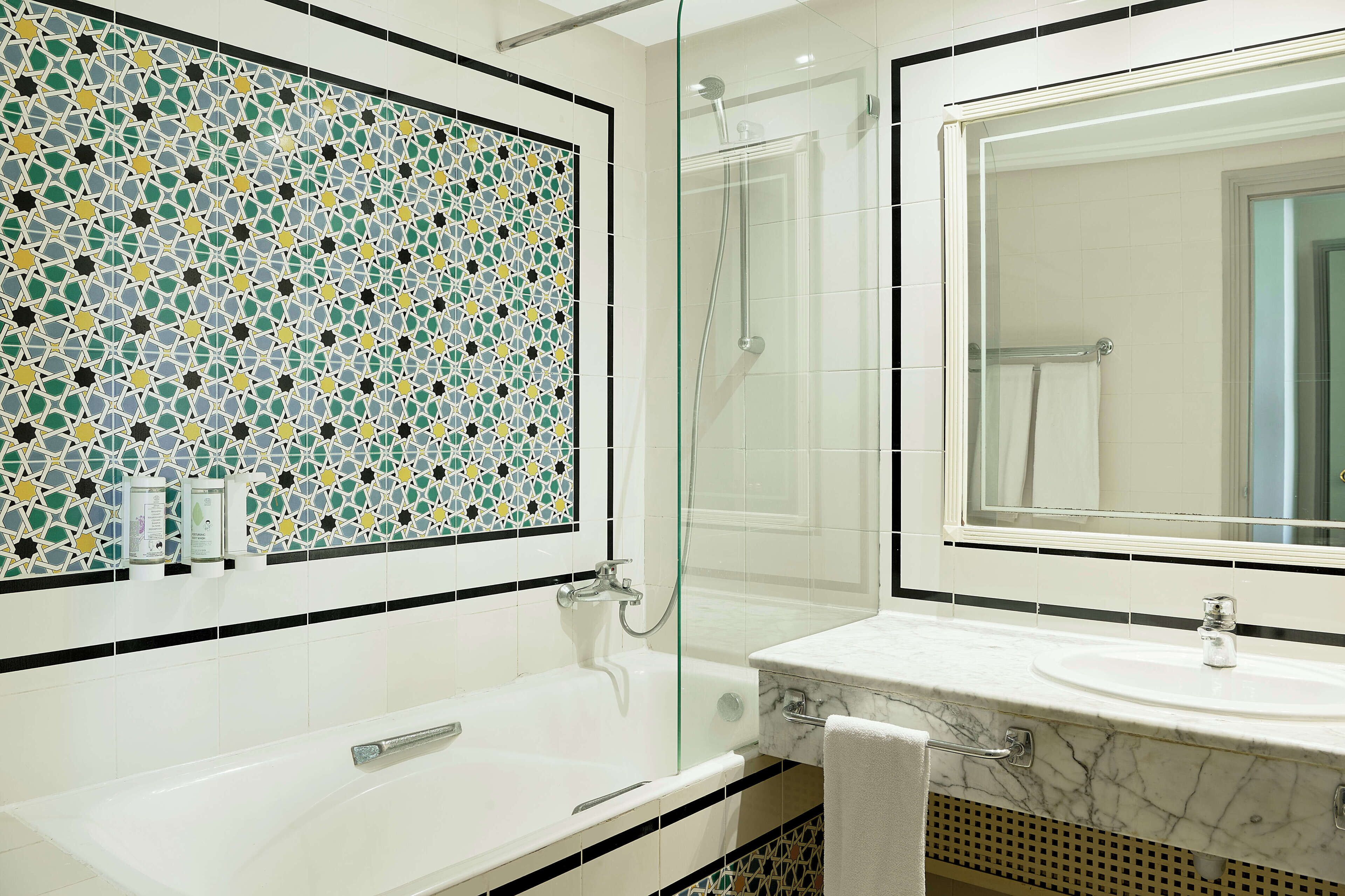 A bathroom with a mosaic tile wall, a glass-enclosed shower, and a marble sink.