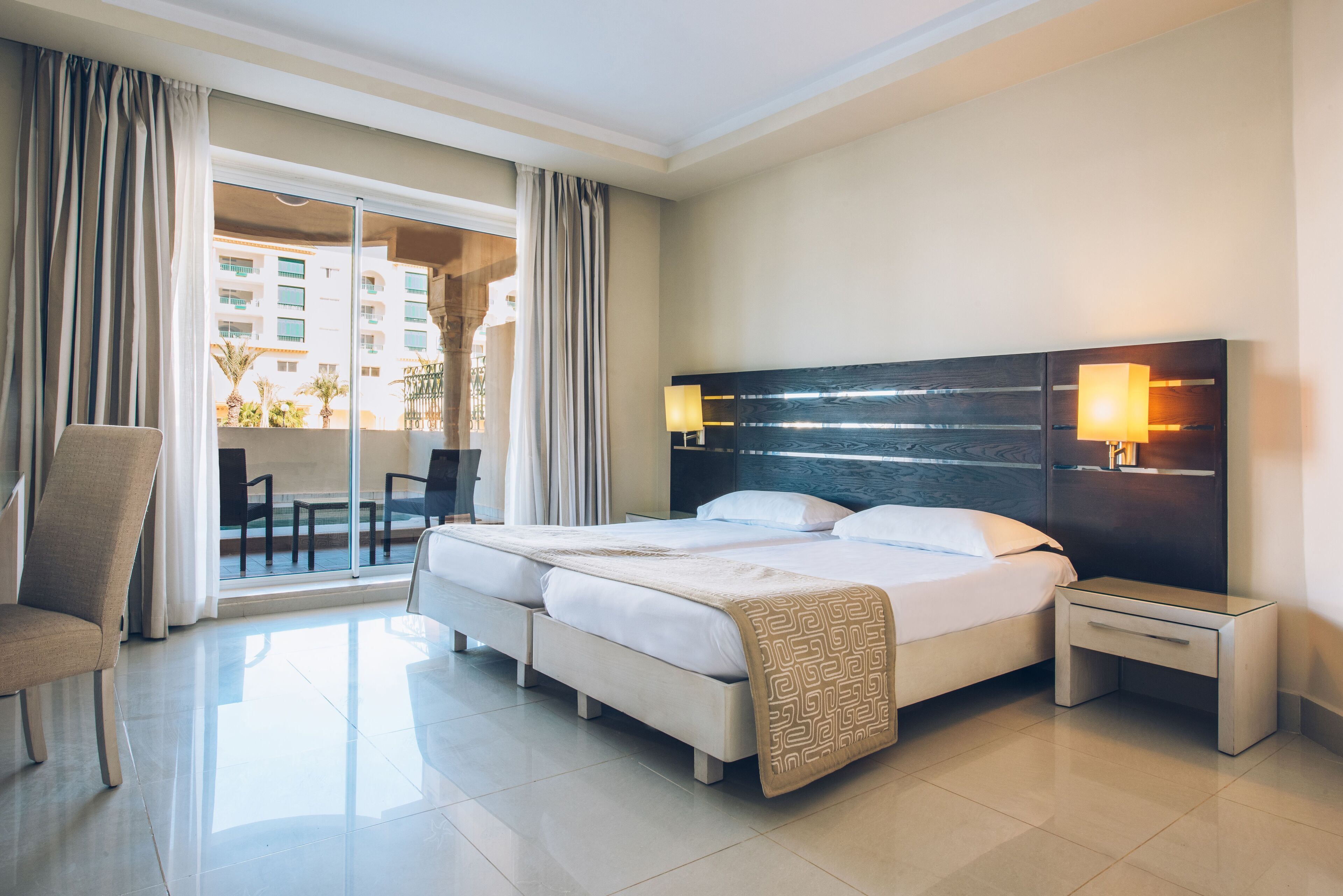 A hotel room with a large bed, two bedside tables, a chair, and a view of the outside balcony.