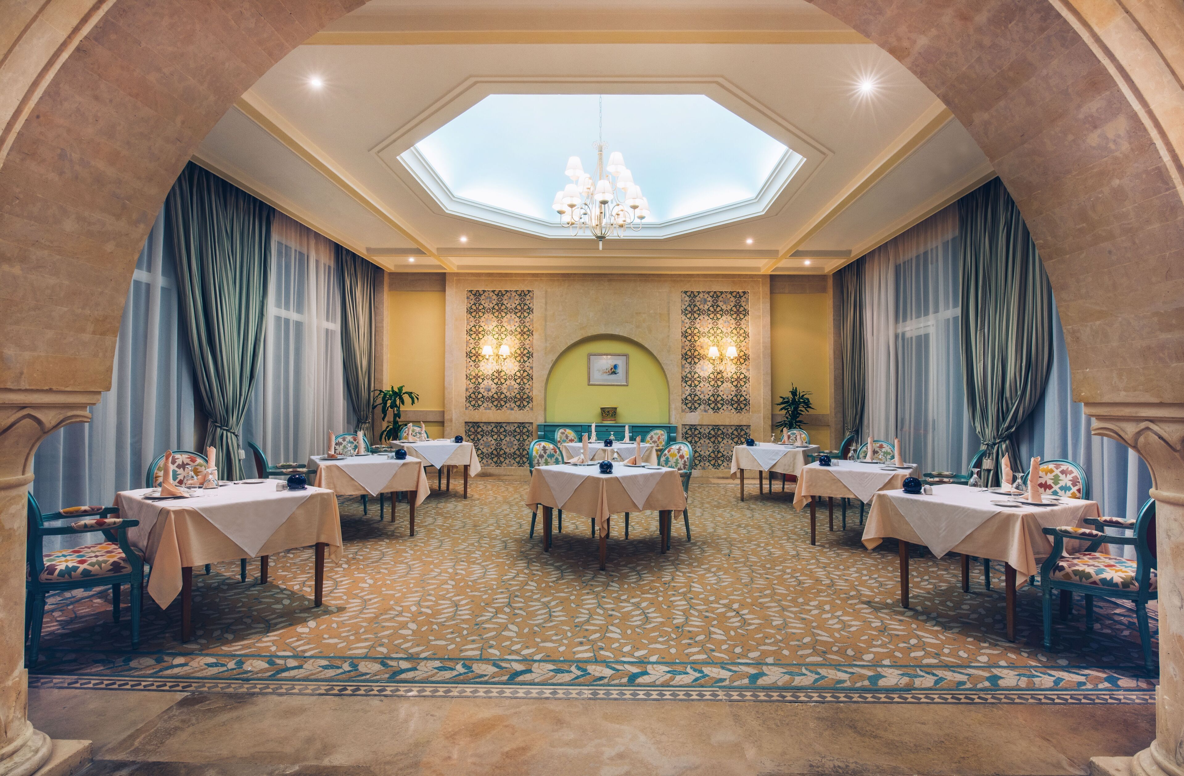 Un comedor amplio con varias mesas y sillas, un candelabro central y un tragaluz.