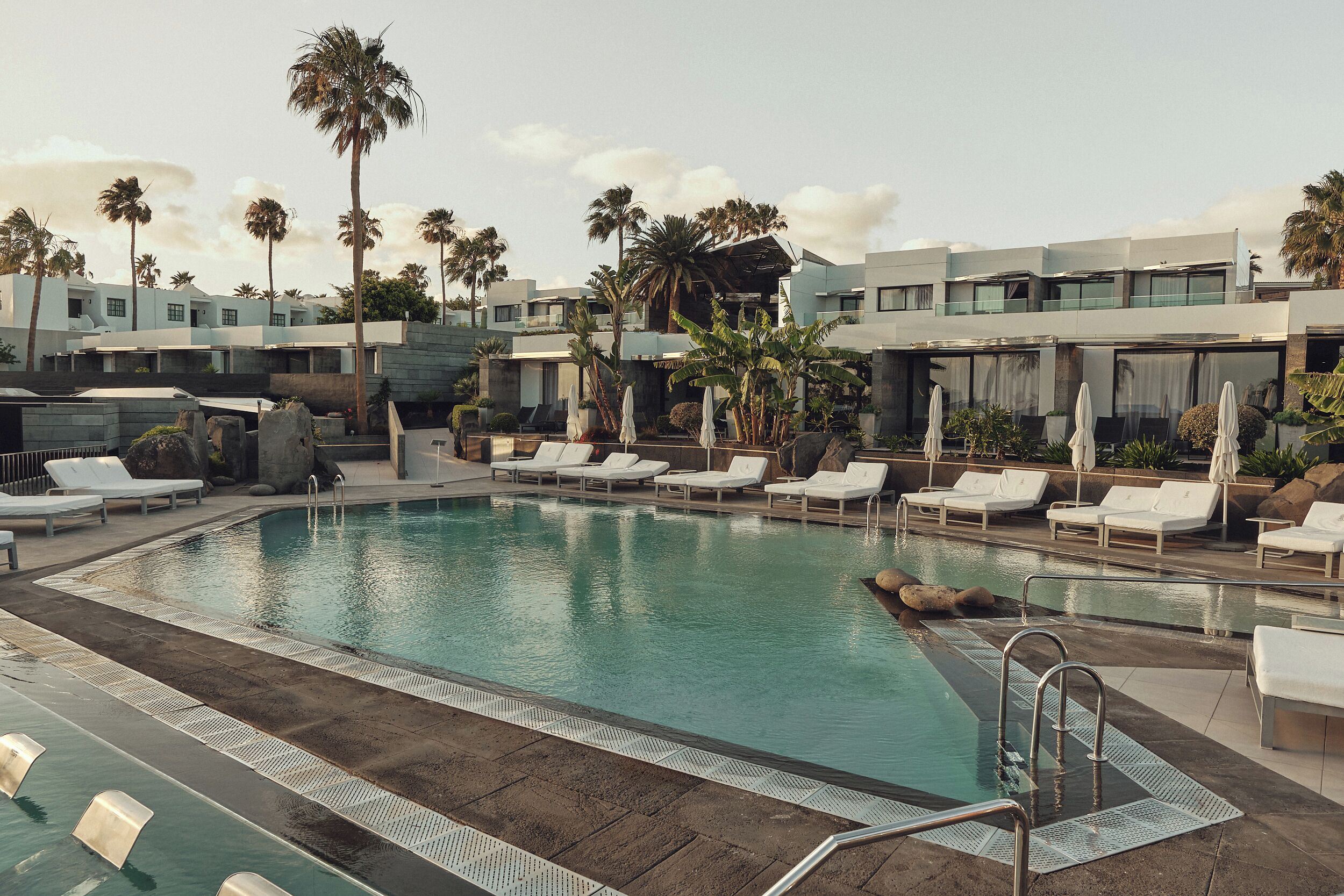 A pool area with lounge chairs and palm trees.