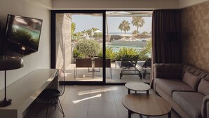 A modern living room with a large TV, a sofa, a coffee table, and a balcony with a pool view. - La Isla y el Mar Hotel Boutique - Adults Only (Tías)