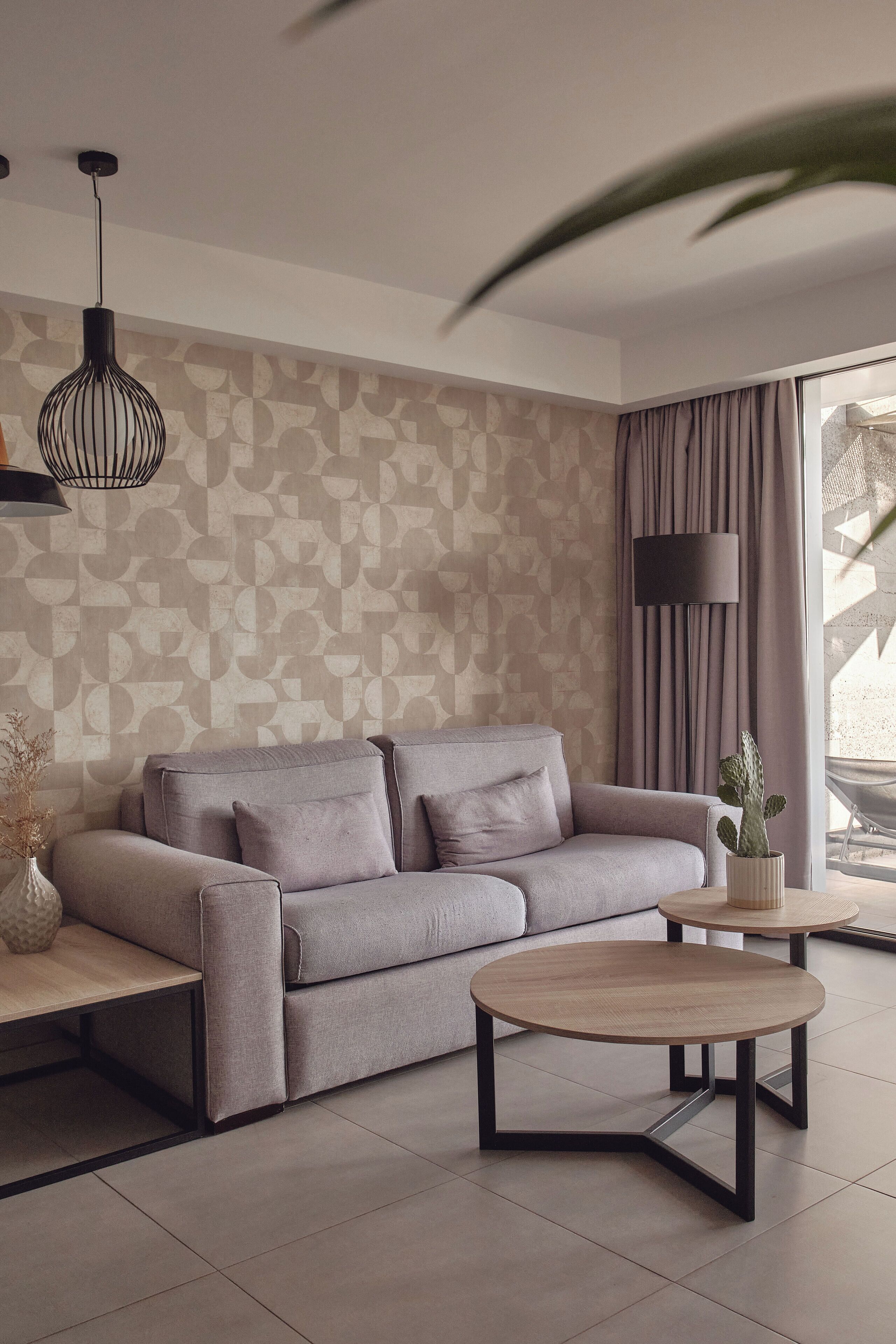 A modern living room with a grey sofa, a round coffee table, and a patterned wall.