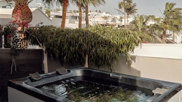 Un jacuzzi con vista a una zona residencial, palmeras y un edificio de fachada blanca.