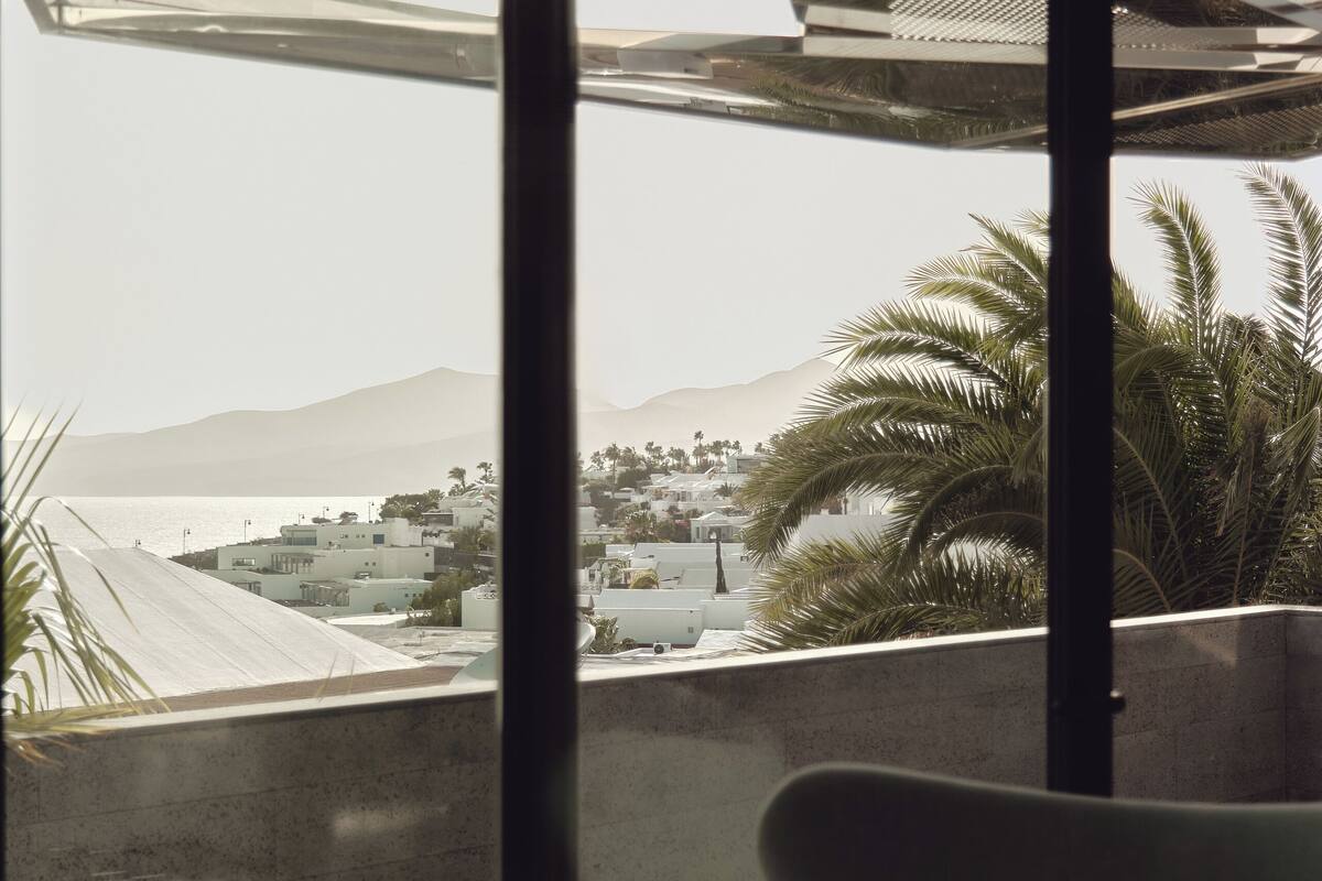 A balcony with a view of a coastal town, palm trees, and mountains.
