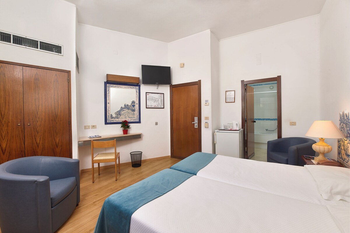 Una habitación de hotel con cama, escritorio, silla, televisor y baño.
