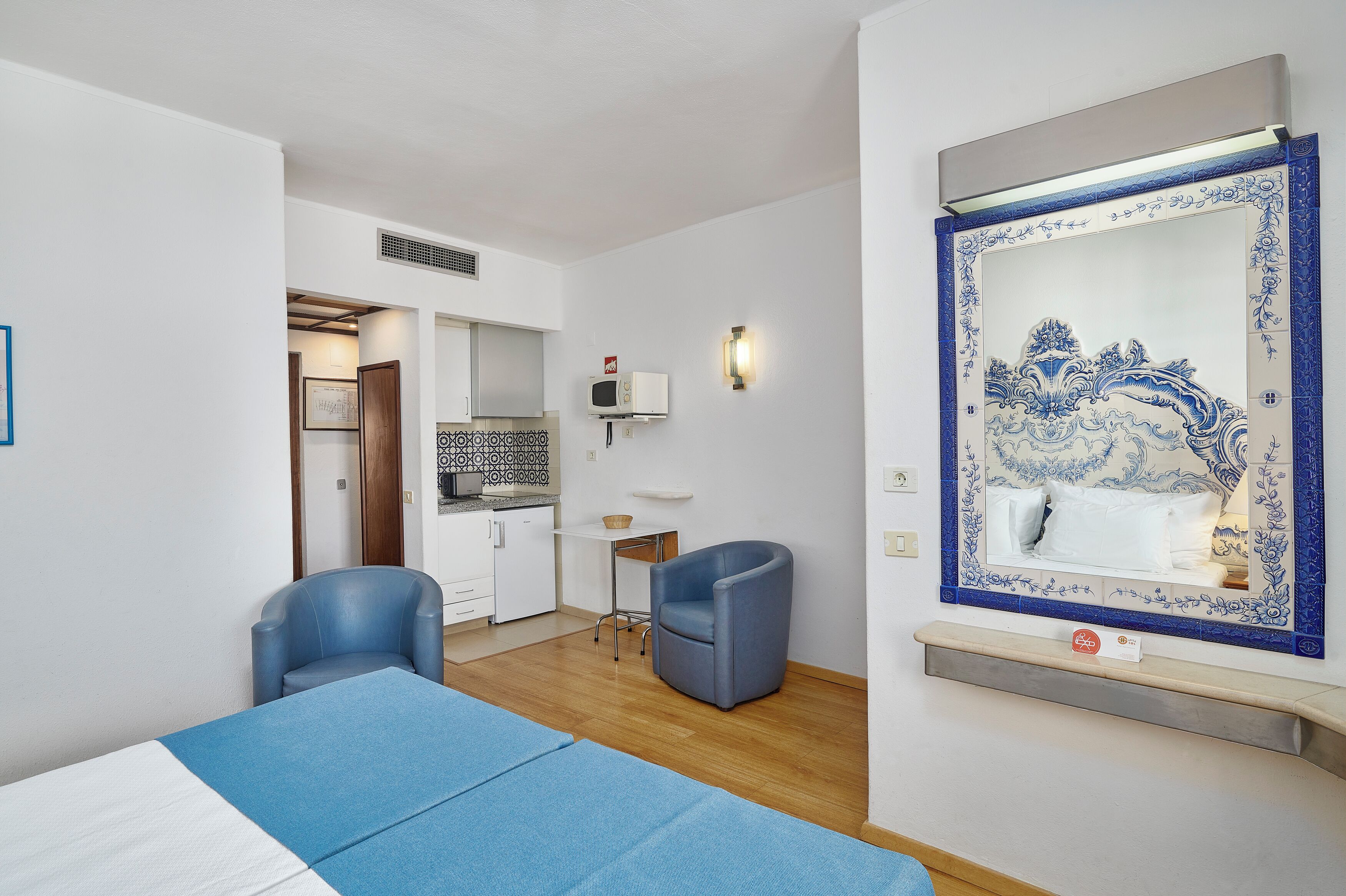 A hotel room with a bed, a desk, a chair, a microwave, and a decorative mirror.