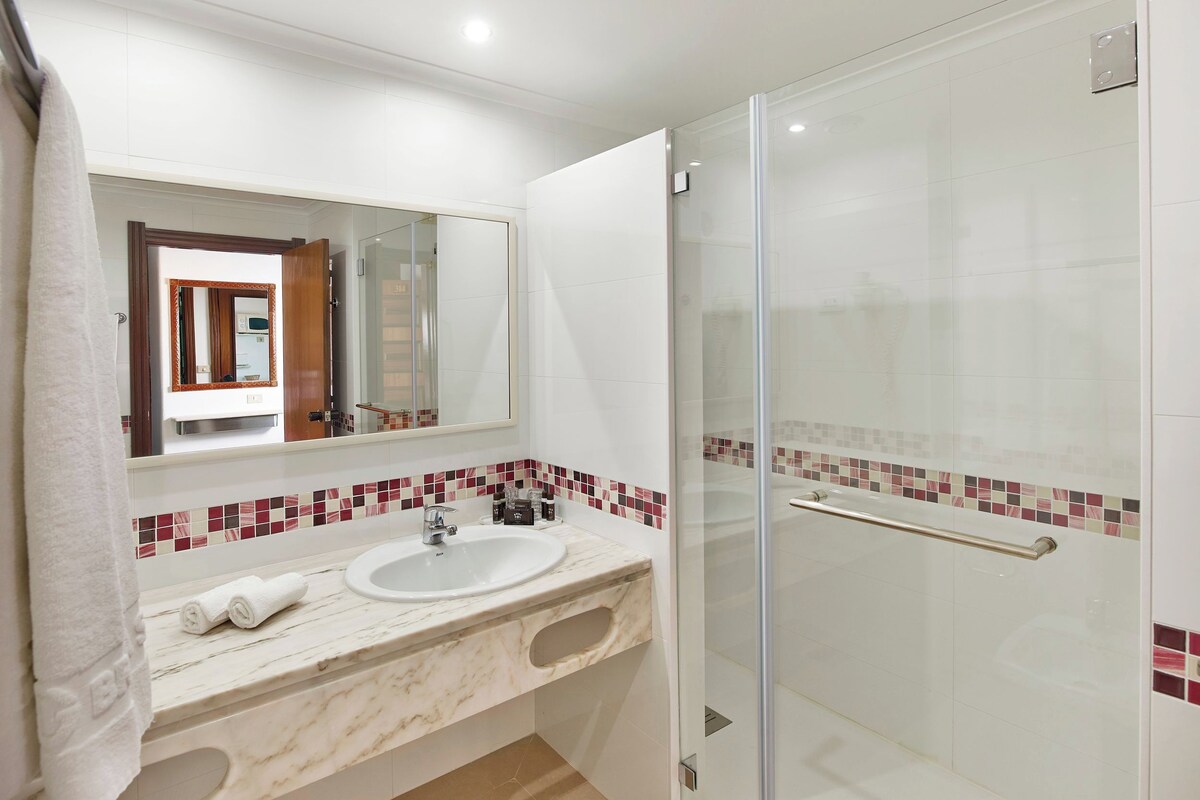 Un baño con lavamanos blanco, espejo y cabina de ducha de vidrio.