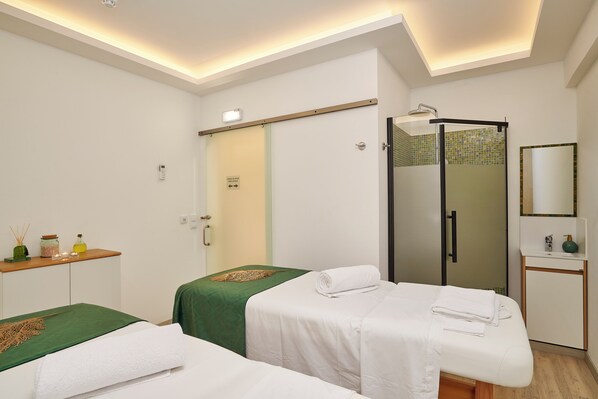 Habitación de hotel con dos camas individuales, un escritorio pequeño con un espejo, zona de ducha y una puerta con un cartel.
