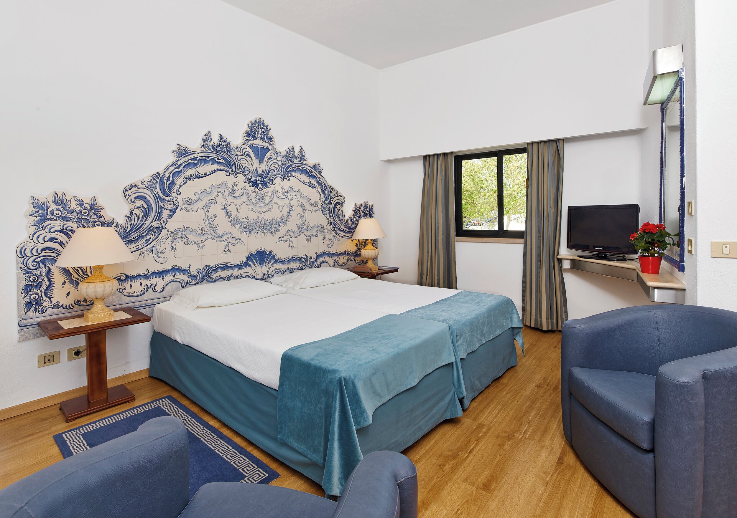 A hotel room with a bed, a desk, a chair, a TV, and a window.